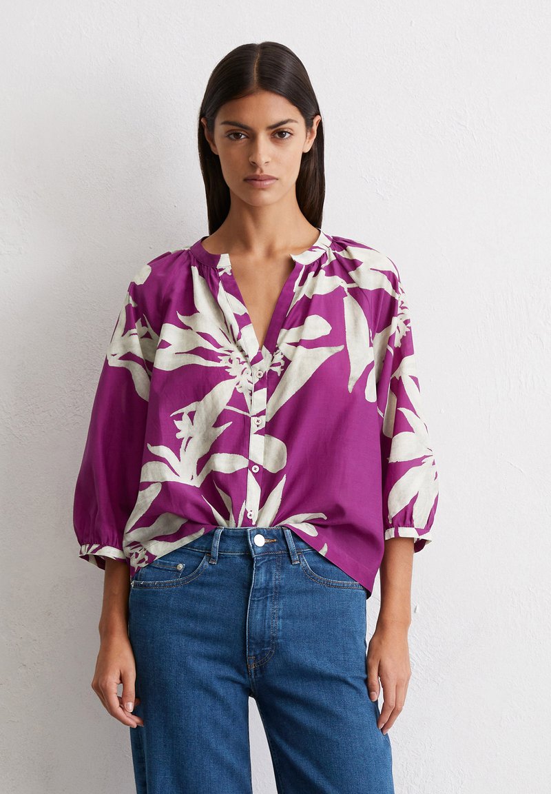 Blouse florale violette avec imprimé botanique blanc, coupe décontractée, design à boutons, col rond et manches trois-quarts. À assortir avec un jean bleu.