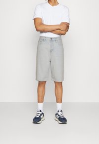 Světlé modré denimové kraťasy se rovný střihem, designem s pěti kapsami a zapínáním na knoflík, doplněné bílým tričkem a tmavými teniskami.