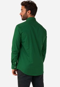 Camicia verde con colletto classico, maniche lunghe e orlo arrotondato, realizzata in un tessuto liscio. Presenta bottoni bianchi sui polsi.