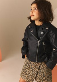 Zwarte leren motorjack met zilverkleurige hardware, gecombineerd met leopard-print shorts. Beschikt over ritszakken en een cropped ontwerp.