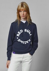 Jūras spēku kapuce ar baltu apļveida tekstu "RED BULL RACING". Iekļauj stiepjamu kapuci un ribotu piedurkņu galus. Apvienots ar baltām džinsiem.