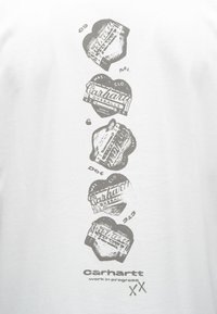 Biała koszulka z pionowym wzorem czarnych vintage'owych metek, z tekstem i logo Carhartt oraz graficznymi akcentami na dole.