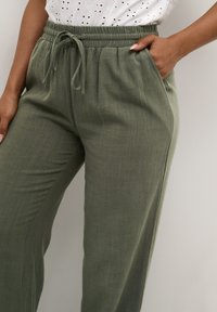 Olive green, lightweight fabric pants with an elastic waistband, drawstring, and side pockets, featuring a relaxed fit and subtle texture.