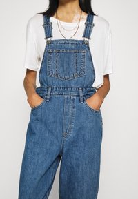 Jeansoverall med justerbara axelband, framficka och sidofickor. Avslutad i en medelblå tvätt med en avslappnad passform.