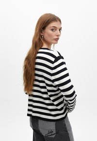 Pasiasty sweter w czarno-białym kolorze, wykonany z miękkiej tkaniny, z długimi rękawami i luźnym krojem. Szare dżinsy z haftowanym detalem na kieszeni.