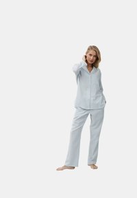 Lichtblauw en wit gestreept pyjama set bestaande uit een knoopsluiting top met een borstzak en losse broek met rechte pijpen.