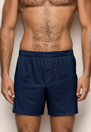 Marineblaue Baumwollunterhosen mit elastischem Bund, zwei Knöpfen am Flug und glatter Textur. Keine Muster oder zusätzliche Hardware sichtbar.