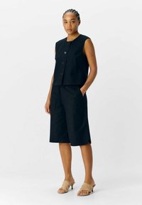 Zwarte mouwloze top met knopen aan de voorkant en bijpassende knielange shorts. De stof is soepel, heeft zijzakken en een ontspannen pasvorm.