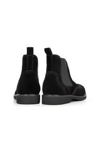 Černé suede kotníkové boty s elastickými bočními panely, poutky na stažení a hladkou gumovou podrážkou. Obsahují kontrastní prošívání a elegantní design.
