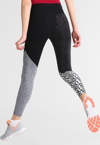 Leggings neri e grigi con un motivo geometrico, dotati di un alto cinturino in vita e design a blocchi di colore. Abbinati a scarpe grigie con accenti arancioni.