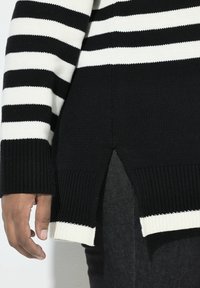 Maglione a strisce bianche e nere in maglia con orlo a coste e dettaglio con fessura laterale, caratterizzato da maniche lunghe e tessuto testurizzato.
