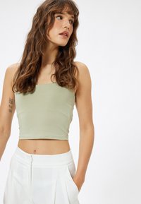 Top corto verde claro de algodón suave, con escote cuadrado y diseño ajustado, combinado con pantalones plisados blancos de cintura alta.