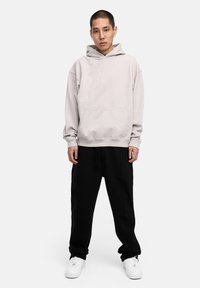 Hellgrauer Kapuzenpullover mit Kängurutasche, über schwarzen Jogginghosen und weißen Sneakern. Lässiger Schnitt, weicher Stoff und lange Ärmel.