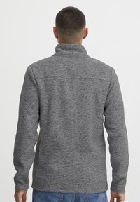 Pullover grigio in fleece con colletto alto, tessuto strutturato, maniche lunghe e vestibilità rilassata. La vista posteriore mostra i dettagli delle cuciture sulle spalle.