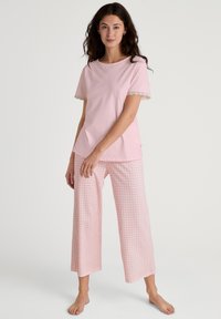 Roze katoenen t-shirt met kantafwerking aan de mouwen, gecombineerd met wijde broek met een roze en witte ruitpatroon.