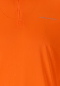 Kirkas oranssi lyhythihainen paita, jossa on vetoketjullinen kaulus, valmistettu teksturoidusta kankaasta ja jossa on heijastava logo etupuolella.