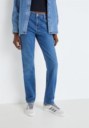 Jeans en denim bleu clair avec une coupe droite, dotés d'une fermeture à bouton et de détails de couture subtils. Associés à des baskets grises.
