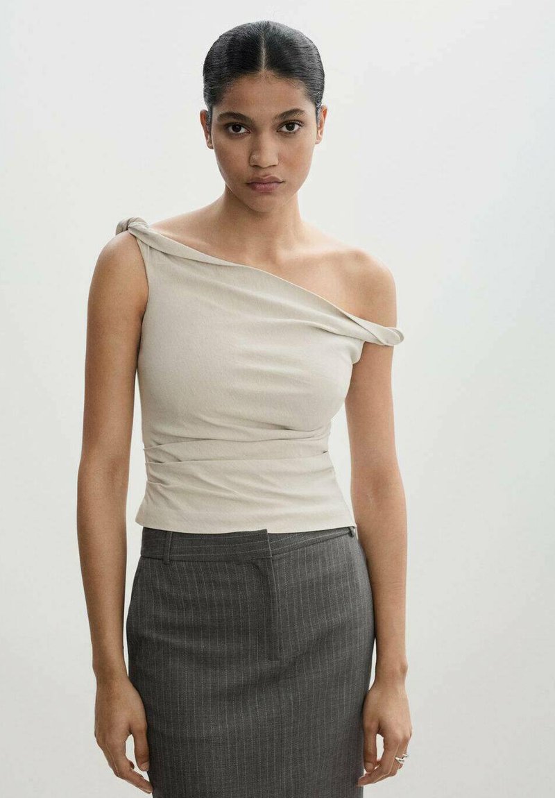 Top beige de un solo hombro con tejido drapeado, diseño ajustado y textura suave, combinado con una falda lápiz de rayas oscuras.