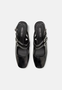 Zapatos de charol negro tipo slingback con puntera cuadrada, que presentan tres correas decorativas y hebillas de plata en el tobillo.