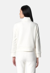 Felpa bianca con colletto, maniche lunghe e polsini aderenti; presenta una texture liscia e un design minimalista.