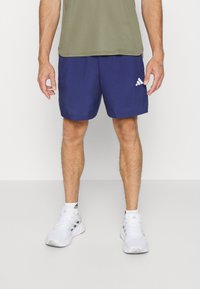 Navy athletic shorts with an elastic waistband and white Adidas logo, paired with white sport shoes and an olive green t-shirt.