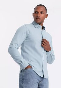Lichtblauwe overhemd met lange mouwen en een button-down kraag, van een textiel met textuur, en aansluitende manchetten, gedragen met casual spijkerbroek.