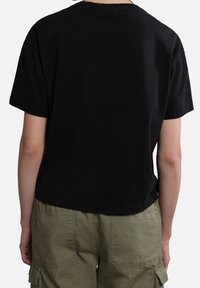 Svart bomullströja med korta ärmar och rak skärning, kombinerad med olivgröna cargobyxor med synliga fickor och en texturerad yta.