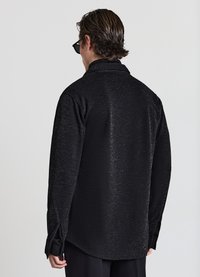 Camicia nera con un motivo testurizzato sottile, design aderente con colletto e maniche lunghe. Spacchi laterali vicino all'orlo per facilitare i movimenti.