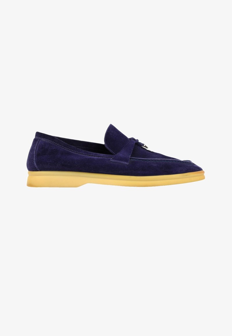 Mocassin en daim bleu foncé avec semelle en caoutchouc marron clair et détail de bride décorative sur le dessus, vu de profil sur fond blanc.