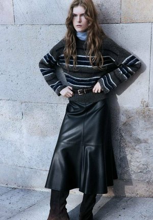 Dunkelgrauer Strickpullover mit weißen und blauen Streifen, kombiniert mit einem schwarzen Leder-Midi-Rock. Braune Wildleder-Stiefel bis zum Knie runden den Look ab.