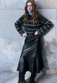 Maglione lavorato a maglia grigio scuro con strisce bianche e blu, abbinato a una gonna midi in pelle nera. Stivali alti fino al ginocchio in camoscio marrone completano il look.