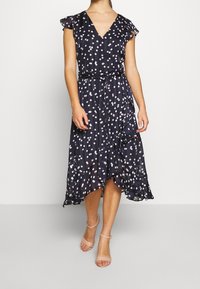 Navy blue dress with pink and white polka dots, V-neck, cap sleeves, and a belted waist. Flowy, knee-length with a ruffled hem.