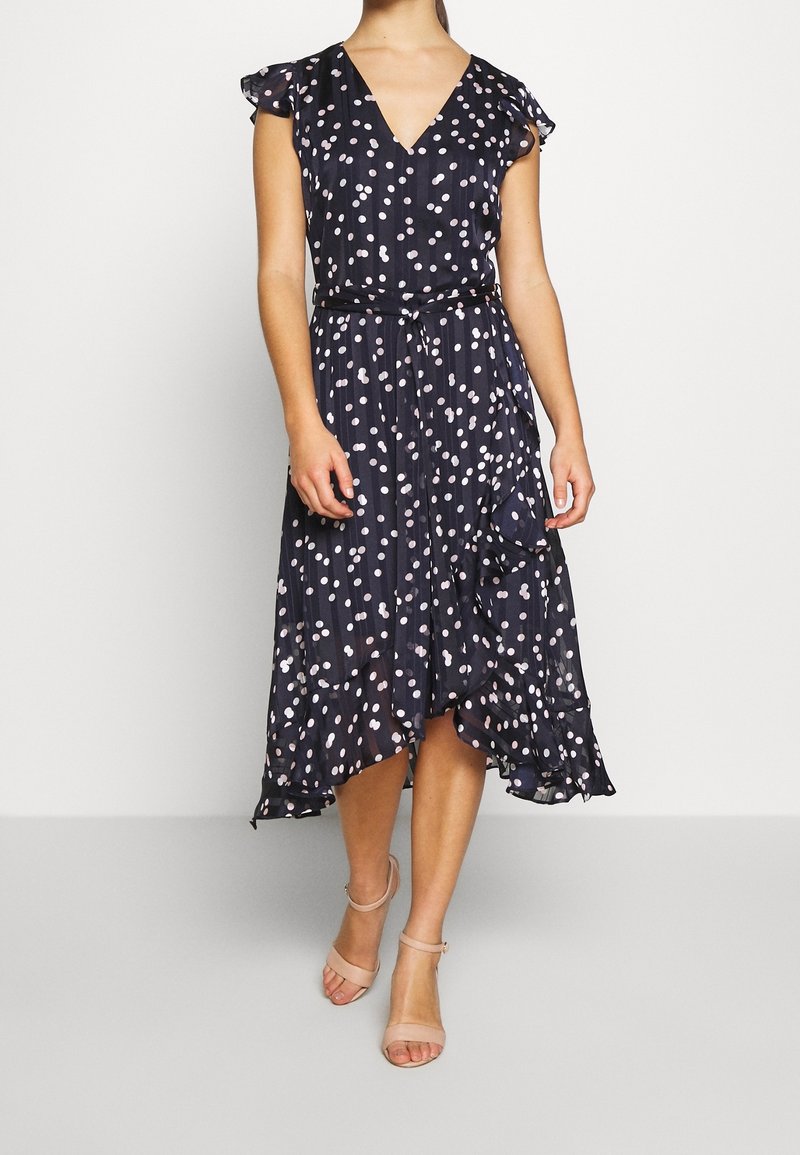Navy blue dress with pink and white polka dots, V-neck, cap sleeves, and a belted waist. Flowy, knee-length with a ruffled hem.