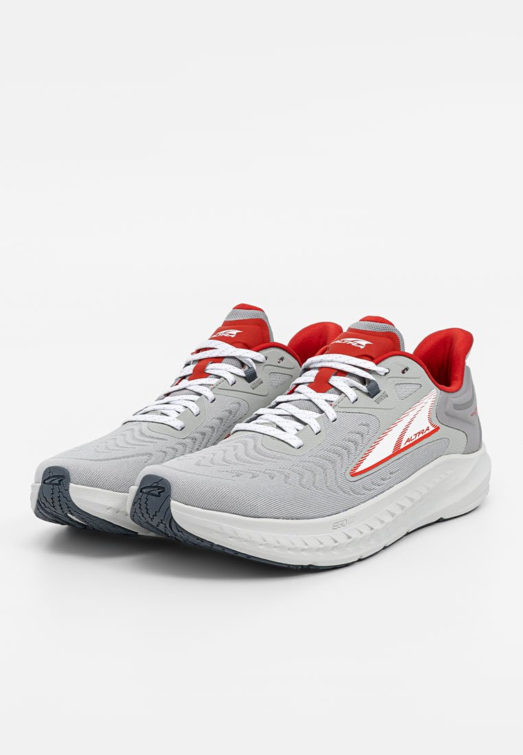 Zapatilla deportiva con parte superior de malla gris, acentos rojos y cordones blancos. Cuenta con una suela acolchada y una banda de rodadura texturizada para agarre.