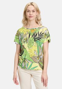 Bluzka z krótkim rękawem w jasnym zielonym i żółtym tropikalnym wzorze liści. Lekki materiał o luźnym kroju i okrągłym dekolcie.