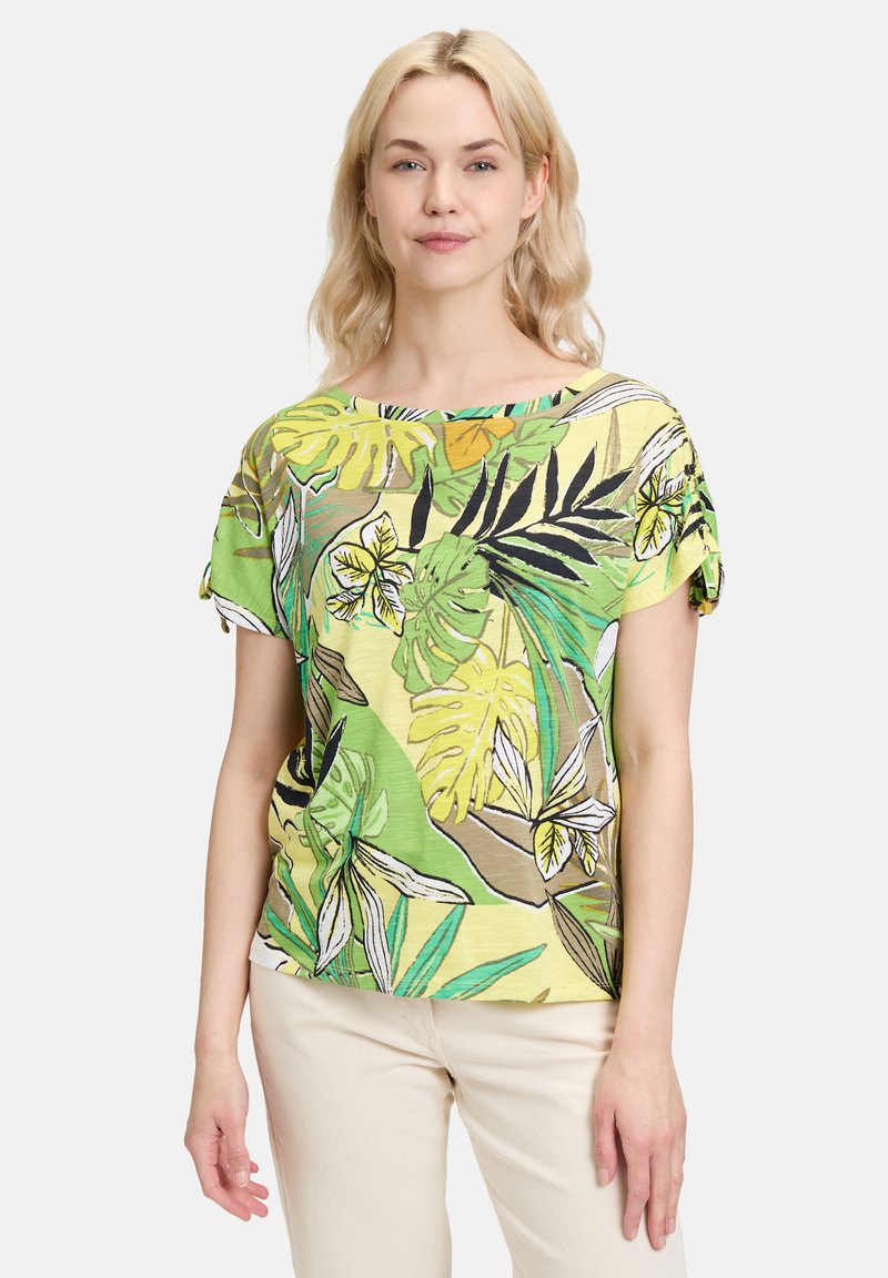 Bluzka z krótkim rękawem w jasnym zielonym i żółtym tropikalnym wzorze liści. Lekki materiał o luźnym kroju i okrągłym dekolcie.