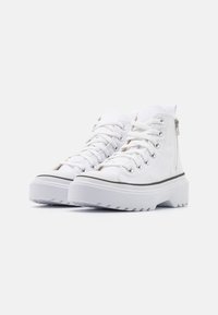 White high-top sneakers with lace-up and side zipper, featuring a thick rubber sole and black accent stripe on the base, canvas material.