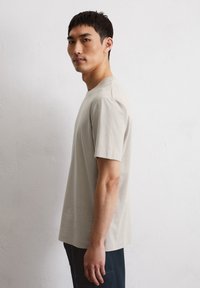 Lichtbeige kortmouw t-shirt van zachte stof, met een klassieke ronde halslijn en een relaxte pasvorm, gecombineerd met donkerblauwe broek.