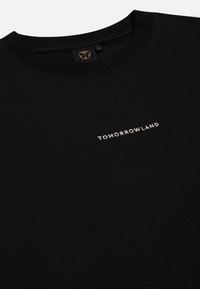 Zwarte katoenen t-shirt met een ronde halslijn, voorzien van een klein goudkleurig gematlegd "TOMORROWLAND" logo op de voorkant. Gladde textuur.
