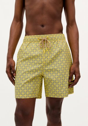 Gelbe Badehose mit einem geometrischen Muster in Grau, ausgestattet mit einem elastischen Bund und einem beigen Kordelzug. Der Stoff wirkt glatt und leicht.