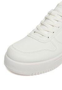 Zapatilla blanca de corte bajo con parte superior de cuero texturizado, cordones blancos a juego y suela gruesa de goma con dibujo.