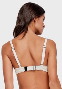 Reggiseno bianco con tessuto strutturato, spalline regolabili e chiusura con fibbia in plastica sul retro. Presenta linee morbide e un design minimalista.