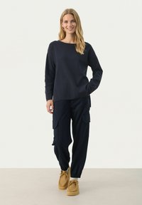 Pull en polaire marine à col rond avec une coupe décontractée, associé à un pantalon cargo marine avec des poches latérales, et des chaussures marron à enfiler.