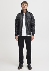 Musta nahasta valmistettu pommittaj jacket, jossa on vetoketjukiinnitys, kaksi rintataskua, ribbatut hihansuut ja olkapäät. Päällä valkoinen t-paita ja mustat housut.