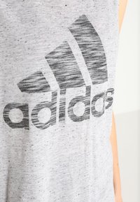 Harmaa hihaton t-paita pehmeää kangasta, jossa on suuri musta Adidas-logo tekstuurilla ja harjatulla efektillä etupuolella.