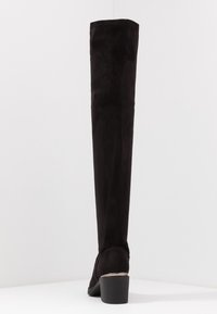 Bota negra por encima de la rodilla hecha de ante, con un tacón grueso y textura suave. Diseño simple, sin patrones visibles ni detalles de hardware.