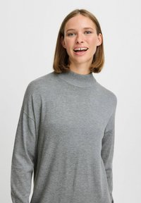 Grijze gebreide trui met een hoge, geribbelde hals en een ontspannen pasvorm. De stof heeft een zachte textuur met subtiele kleurvariaties.