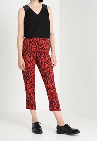 Svart ärmlös topp med pärlprydnader vid axlarna, i kombination med korta byxor i röd djurmönster. Modellen har på sig glänsande svarta snörskor.