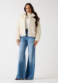 Faux-Fur-Cremejacke mit Kragen und Knopfverschluss, kombiniert mit hoch taillierten, hellblauen Schlagjeans. Glatte Textur.