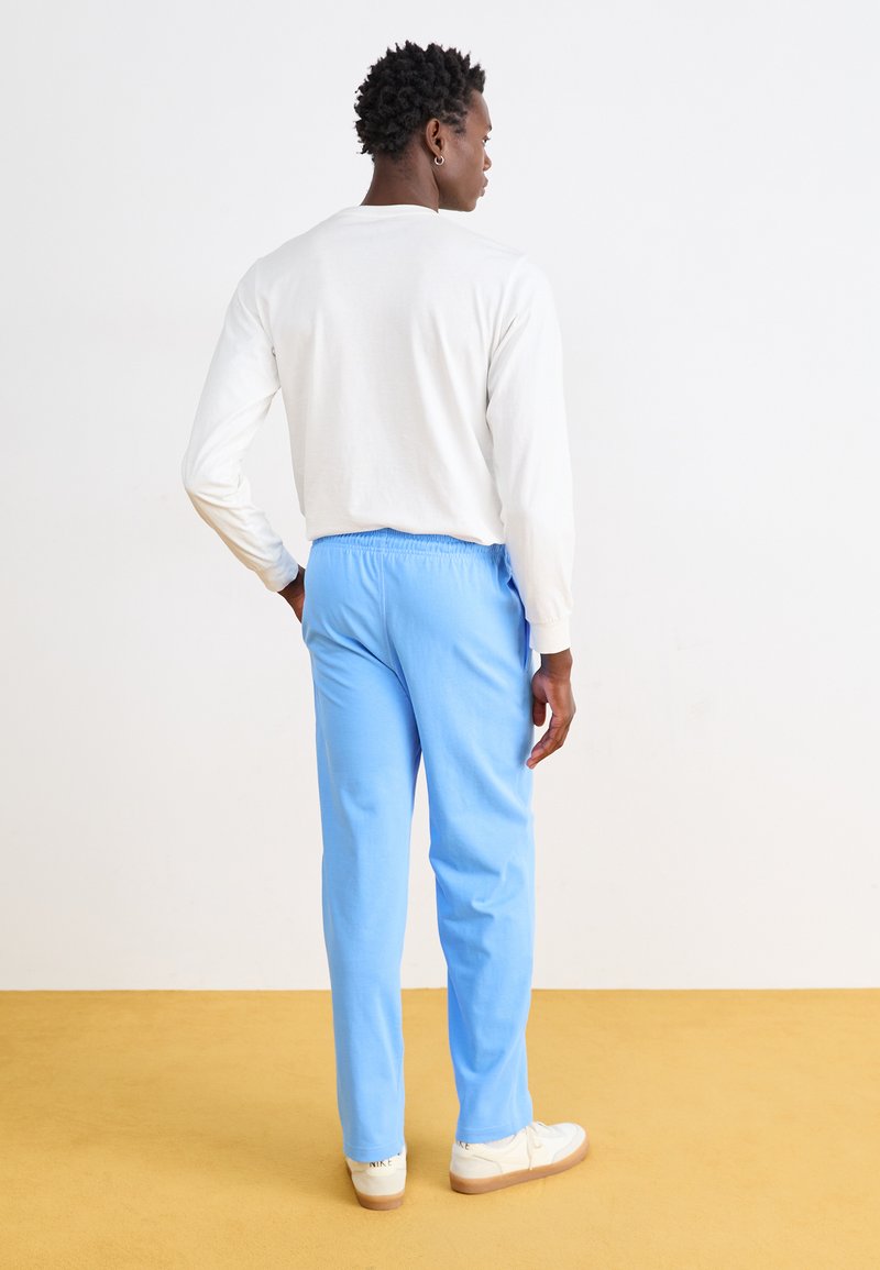 Pantalones azul claro con una cintura elástica, combinados con una camisa blanca de manga larga y zapatillas blancas, vistos desde la parte de atrás.